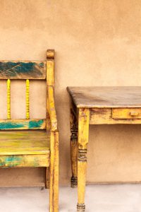Old New Mexico porch (portale) with rustic wood bench, table, and traditional dun-colored adobe stucco.